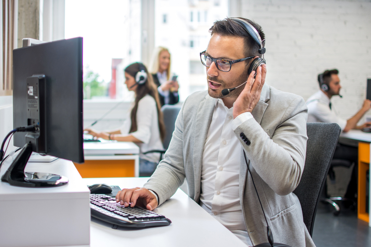 Technical support operator with hands-free headset talking with customer in call center.